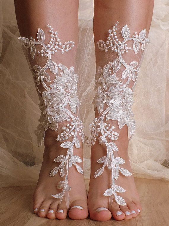 a pair of white lace barefoot sandals are worn on a woman's feet. the sandals are made with delicate floral designs and are very feminine. they are perfect for a wedding or other special occasion.