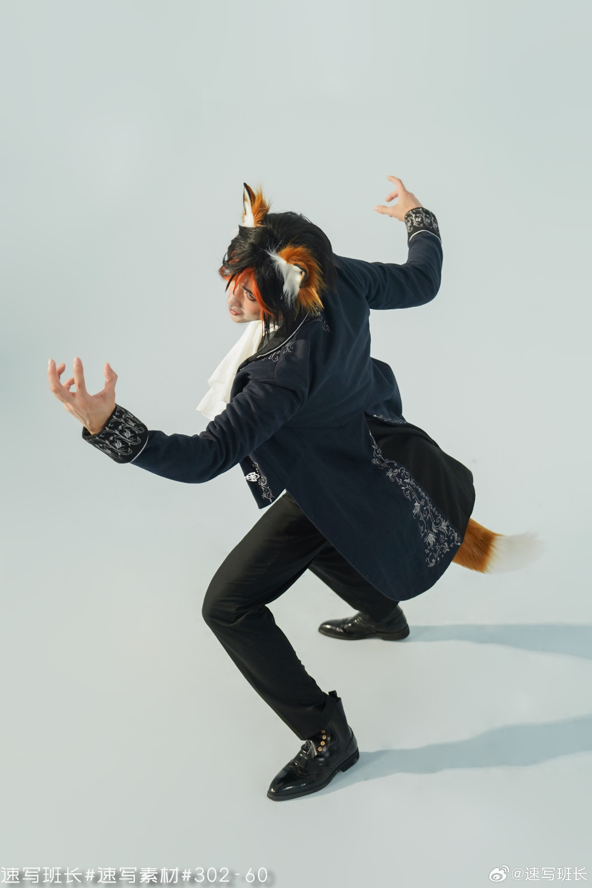 a man in a navy blue coat with floral embroidery and black pants is posing against a light grey background. he wears a white scarf around his neck, a pair of black shoes, and fox ears and a tail as part of a cosplay.  his arms are raised, and his hands are making a clawlike gesture. he appears to be in motion. the image has chinese text at the bottom left corner.