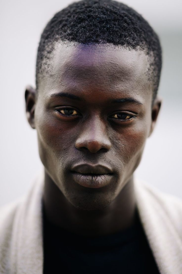 a closeup portrait of a man with dark skin and short hair. he has a serious expression on his face and is looking directly at the camera. the background is a plain white.