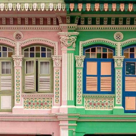 the image shows a closeup view of two adjacent shophouses in singapore, characteristic of peranakan architecture.  the shophouses are painted in contrasting pastel colors—one in a soft pink and the other in a vibrant green.  both feature elaborate details including ornate window frames, decorative tile work along the base of the windows, and columns supporting the upper sections.  the windows have intricately designed shutters, which are partially open. the overall aesthetic is one of rich color, intricate design, and cultural heritage. the buildings appear to be wellmaintained, preserving their historical charm.