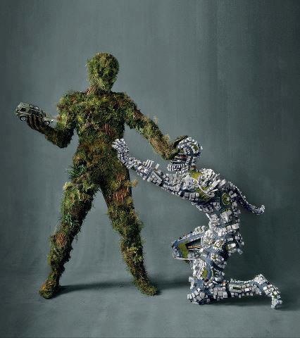 a green man made out of trees and plants looks down at a man made out of a city.  the green man is holding a small car made of metal and wire.