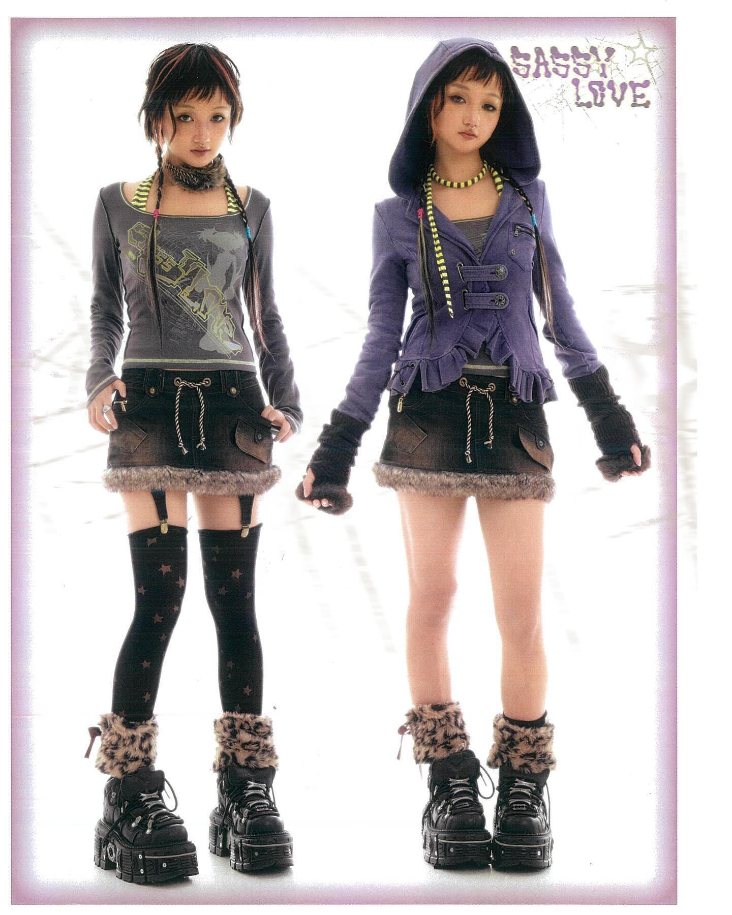 the image shows two young women modeling outfits from the brand "sassy love."  both models are wearing variations of a similar style:  a dark gray graphic longsleeved shirt, a brown mini skirt with faux fur trim,  thighhigh socks with a star pattern, faux fur leg warmers, and chunky platform boots. one model wears a purple hooded jacket.  both have on choker necklaces.  the style is a blend of lolita, street, and grunge aesthetics, typical of japanese fashion trends.  the background is a bright, simple studio setting. the overall vibe is dark and cool.