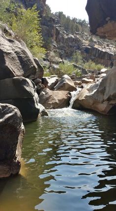 the image shows a stream flowing through a rocky canyon. the water is clear and reflects the sunlight. the rocks are large and irregular in shape, and some are covered with vegetation. the canyon walls are steep and rise high above the stream. the overall impression is one of peace and tranquility.
