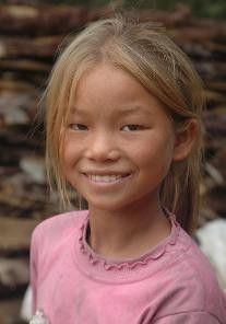 a portrait of a smiling young girl with blonde hair wearing a pink shirt.