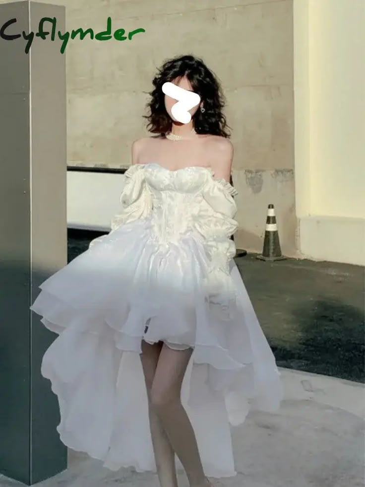 a woman wearing a white offshoulder highlow dress with a tulle skirt, standing outdoors.