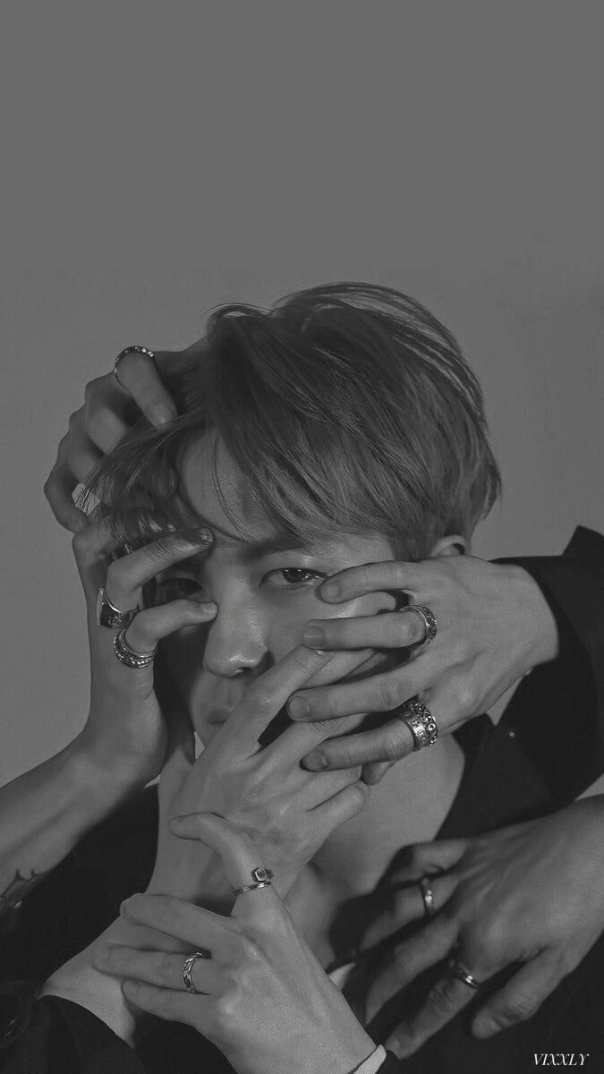 a black and white portrait of a man with his face obscured by his hands, wearing multiple rings on each finger. his expression is intense, and his gaze is piercing. the image is moody and atmospheric, with shadows and light playing on his features. the rings are a striking detail, adding a sense of style and edge to the overall look.