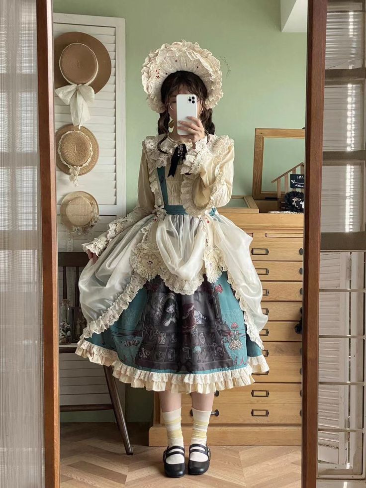 a young woman is posing in a vintageinspired outfit. she's wearing a long, flowing dress with a floral print and a lacetrimmed apron. her hair is styled in curls and topped with a bonnet. she's taking a mirror selfie in a room with wooden floors and furniture.