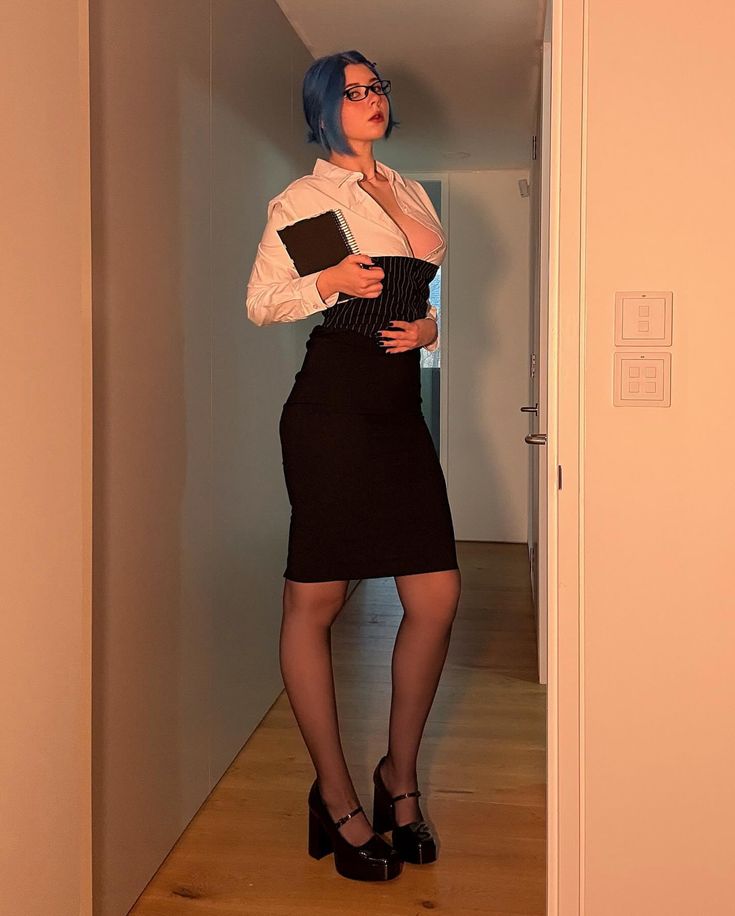 a woman with blue hair and eyeglasses is standing in a hallway. she is wearing a white shirt, a black pencil skirt, a corset, platform shoes, and pantyhose. she is holding a notebook.