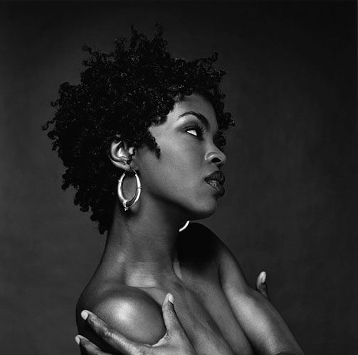 a black and white portrait of a beautiful woman with curly hair. she's wearing a large hoop earring on her left ear. she's looking away from the camera, with her hands crossed in front of her. her face is serene and thoughtful.