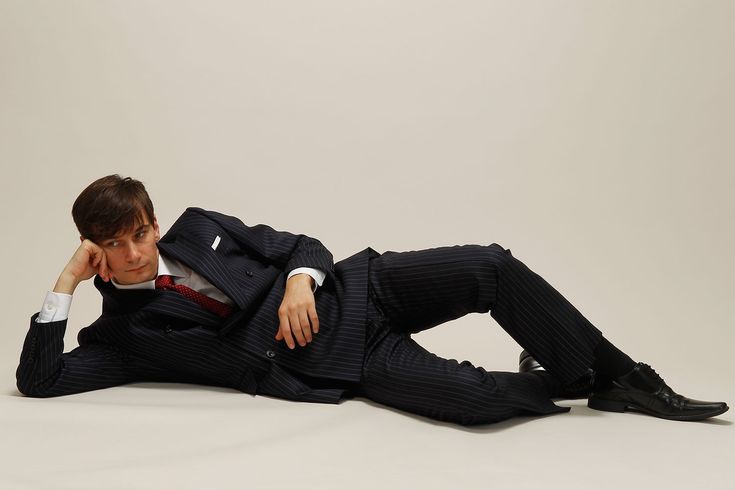 a man in a pinstripe suit is lying down on a white background. he is relaxed and looking off to the side. he has a cool and sophisticated style.