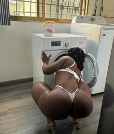 a woman in lingerie is squatting in front of a washing machine in a laundry room.