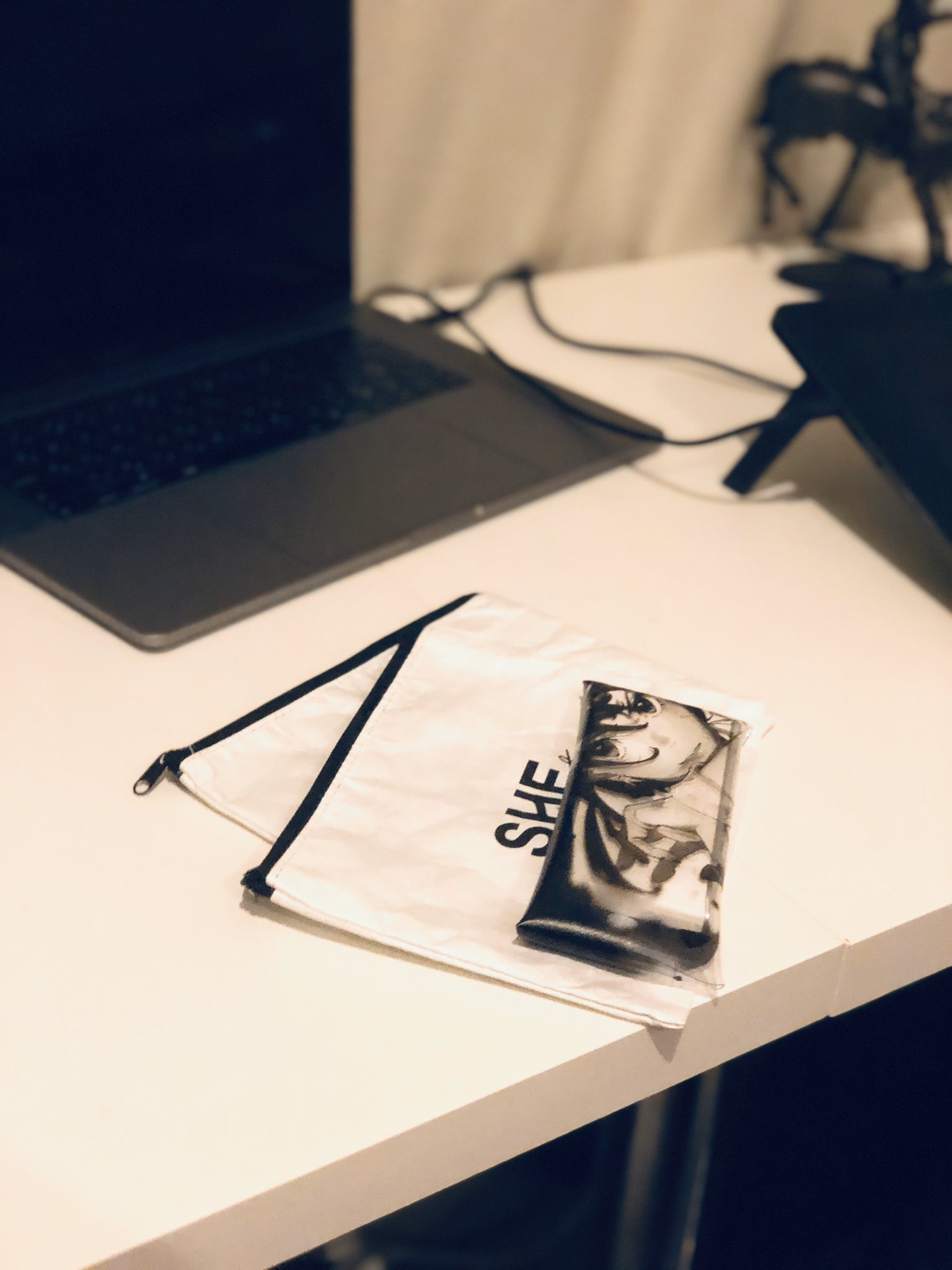 a white desk with a laptop, a white pouch, and a drawing tablet. there is also a black charger connecting the laptop to the drawing tablet.