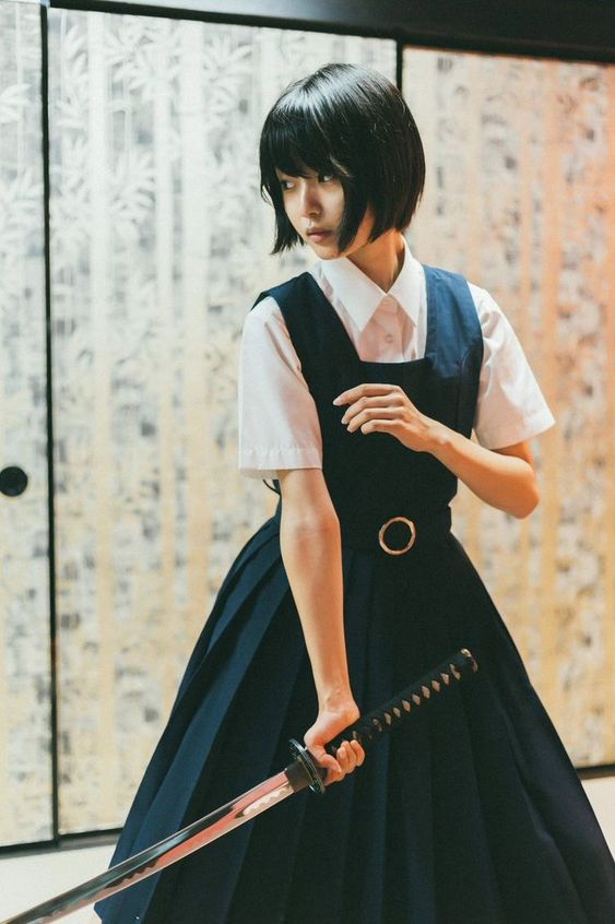 a young woman in a schoolstyle uniform stands poised, holding a katana sword in a traditional japanese room with sliding doors featuring a bamboo forest design. the lighting is soft and natural, creating a cinematic atmosphere.