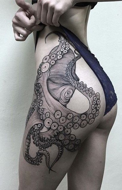 a woman is pictured with an octopus tattoo on her thigh and hip. she is wearing a darkcolored undergarment. the tattoo is black ink and features detailed shading and line work. her hand is also visible.
