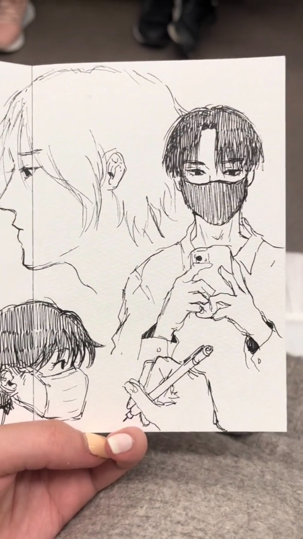 this image is a black and white handdrawn sketch of three anime characters. the focus is on the middle character, a male character with short, black hair, wearing a face mask, and holding a phone. the character to the left has long, blonde hair and is looking at the phone. the character to the right has short, black hair and is wearing a black mask. the drawing is done in pen and ink and is very detailed. the image is held up by a hand.