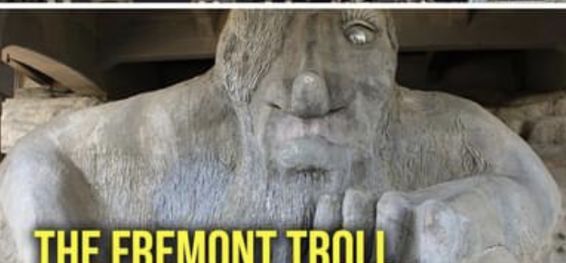 the image shows the fremont troll, a public sculpture located in the fremont neighborhood of seattle, washington. the troll is depicted as a large, grotesque creature with a single eye and a volkswagen beetle crushed under its hand. the sculpture is made of concrete and steel and is a popular tourist destination.