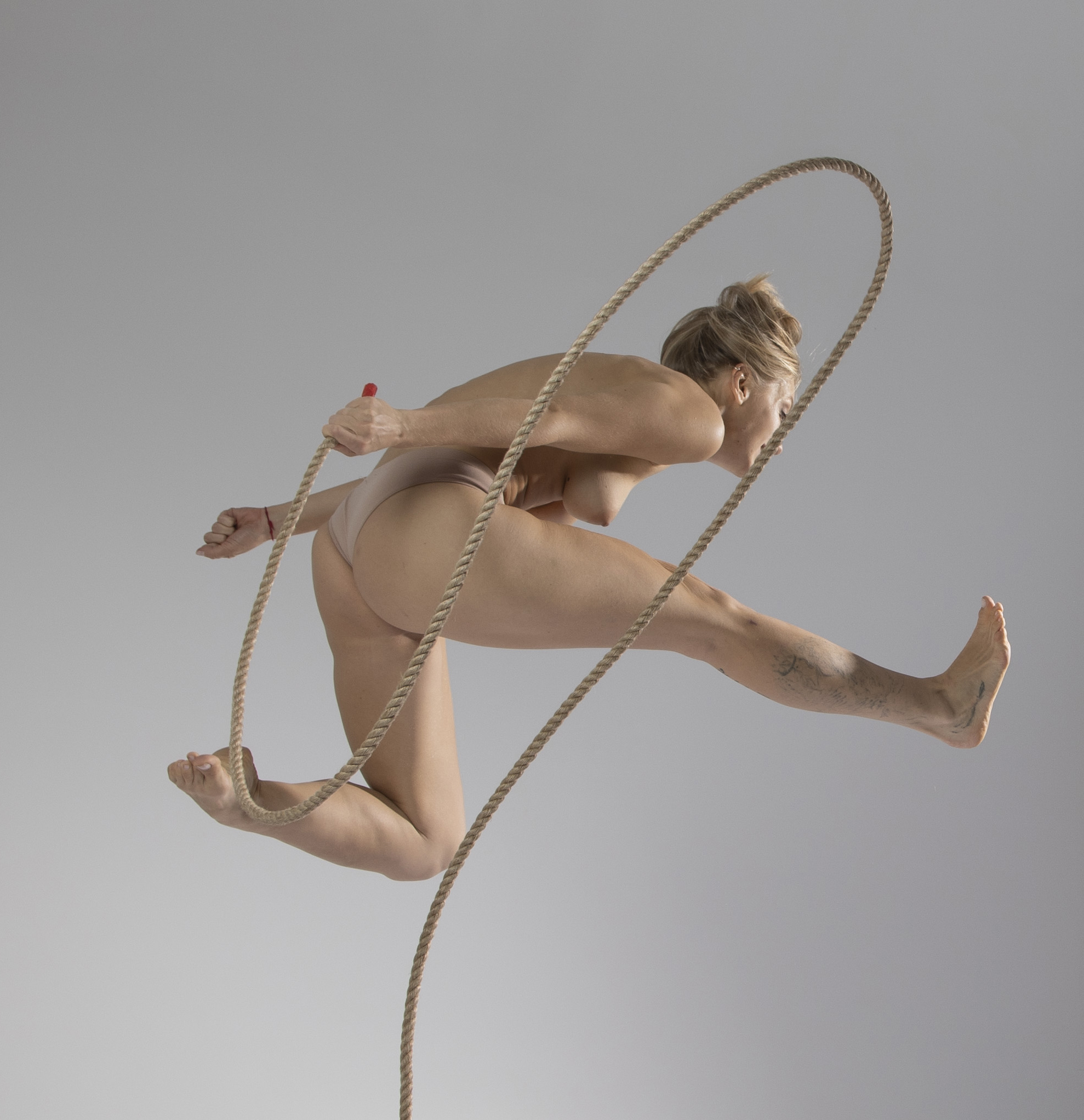 a nude woman is jumping through a hula hoop made of rope. she is athletic and fit, and the image is body positive.