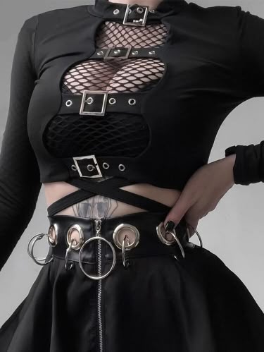 this image features a young woman dressed in a gothic style outfit. the outfit includes a black longsleeved crop top with a mesh panel, a black skirt with a zipper and silver buckles, and a black belt with large silver rings. the outfit is edgy and stylish, with a grunge aesthetic.