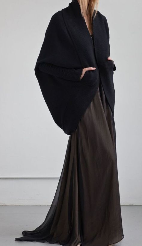 a woman wearing a black dress with long sleeves. she is standing and posing for the camera. the dress is elegant and formal. the fabric is flowing and graceful. the woman is beautiful and stylish.