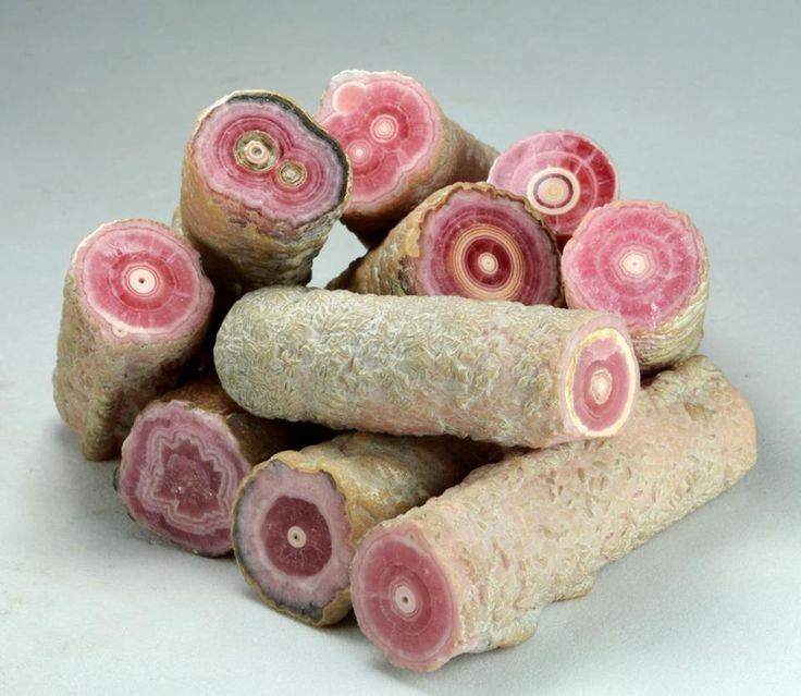 the image displays a collection of rhodochrosite mineral samples. these rocks are cylindrical and exhibit distinct circular patterns on their crosssections. the dominant color is pink, arranged in concentric bands. the outer surface has a rough, unpolished texture.