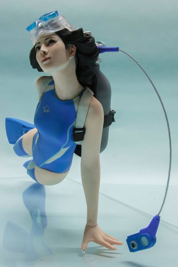 a close up of a detailed figurine sculpture of a woman wearing a blue swimsuit with a diving mask on her face. she is holding a blue diving tank behind her back and has flippers on her feet. the sculpture is placed on a clear reflective surface with a light blue background.