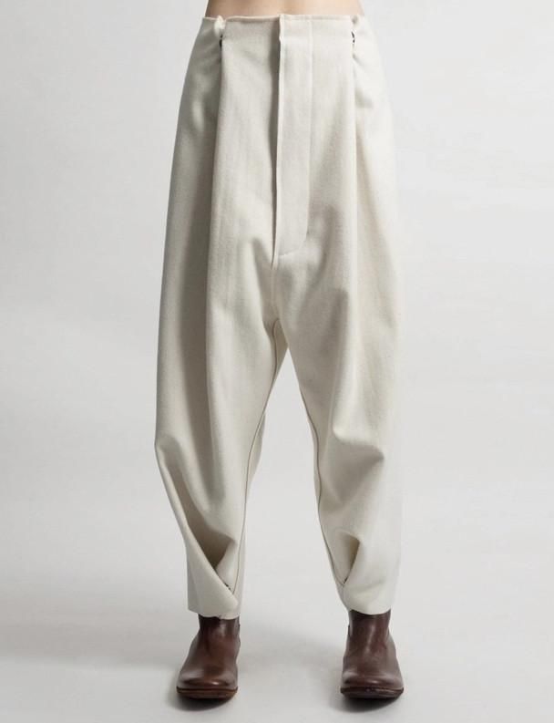 a man is wearing a pair of widelegged, offwhite pants with a loose fit. the pants have a gathered effect at the waist and a slightly tapered leg, and they fall just above the ankle. the man is also wearing brown ankle boots. the pants are a stylish and contemporary choice for a casual outfit.