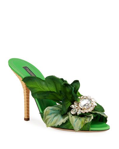 a pair of dolce & gabbana green mules are shown in the image. the shoes are high heels with a floral design featuring green leaves and a crystal embellishment. the shoes are elegant and stylish, suitable for summer wear.