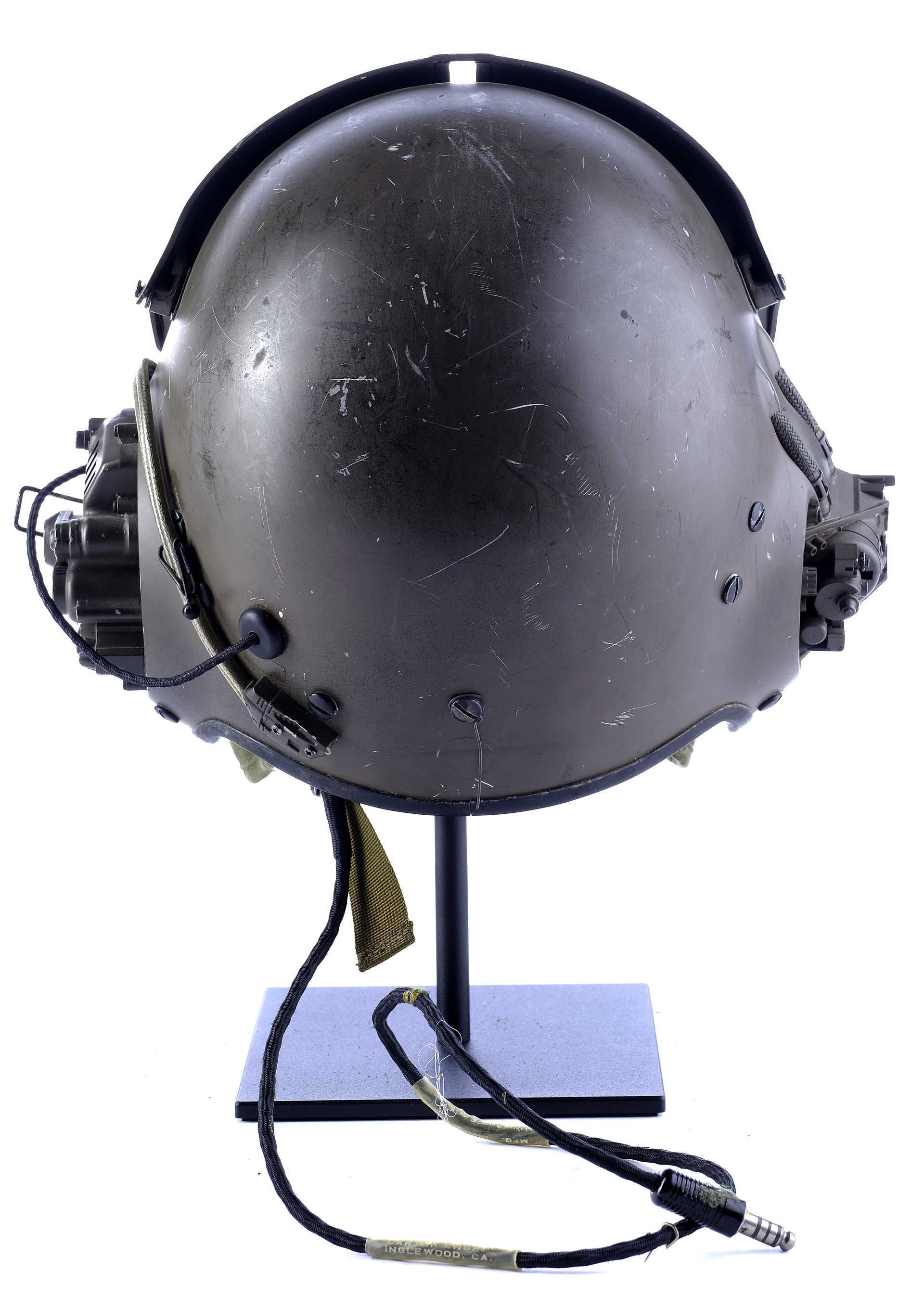 a vintage military flight helmet with a dark green exterior and a black cord.  the helmet is mounted on a black stand, and it is sitting on a blue base. the helmet is in pristine condition.