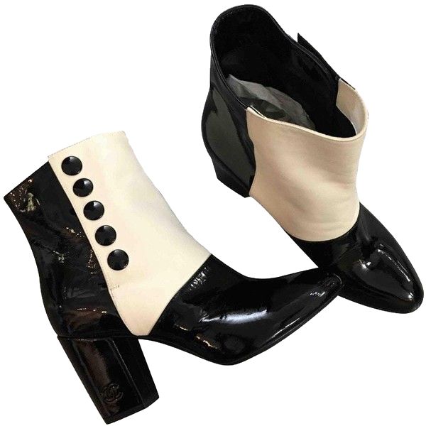 a pair of chanel ankle boots in black and offwhite patent leather. the boots feature a block heel and buttons down the side.  they are shown from a slightly elevated angle, with one boot positioned slightly in front of the other. the image is clean and welllit, showcasing the details of the shoes.