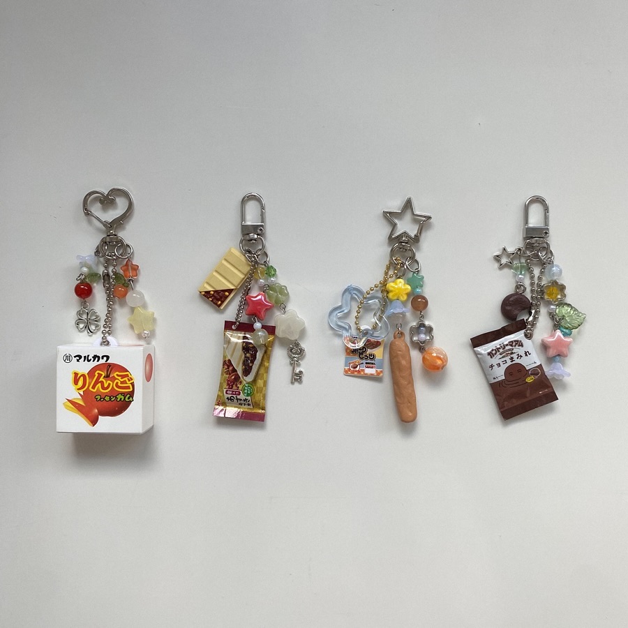 four foodthemed keychains are arranged horizontally on a white background. the keychains feature miniature replicas of various candies and pastries, along with colorful beads and charms shaped like stars, hearts, and flowers.