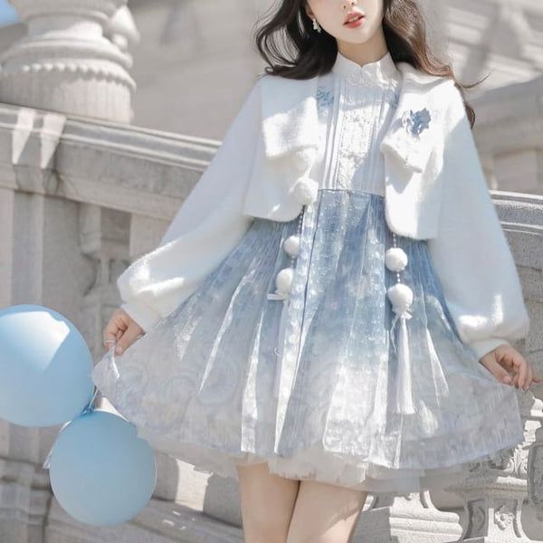 a young woman poses outdoors in a stylish winter outfit. she is wearing a white bolero jacket with fuzzy trim over a blue and white dress with a print of snowflakes and a gradient effect. her outfit is in the lolita fashion style, which is characterized by its dolllike and feminine aesthetic. she is also holding two light blue balloons. the background is a city street with white stone railings and walls. the image is brightly lit with natural daylight.
