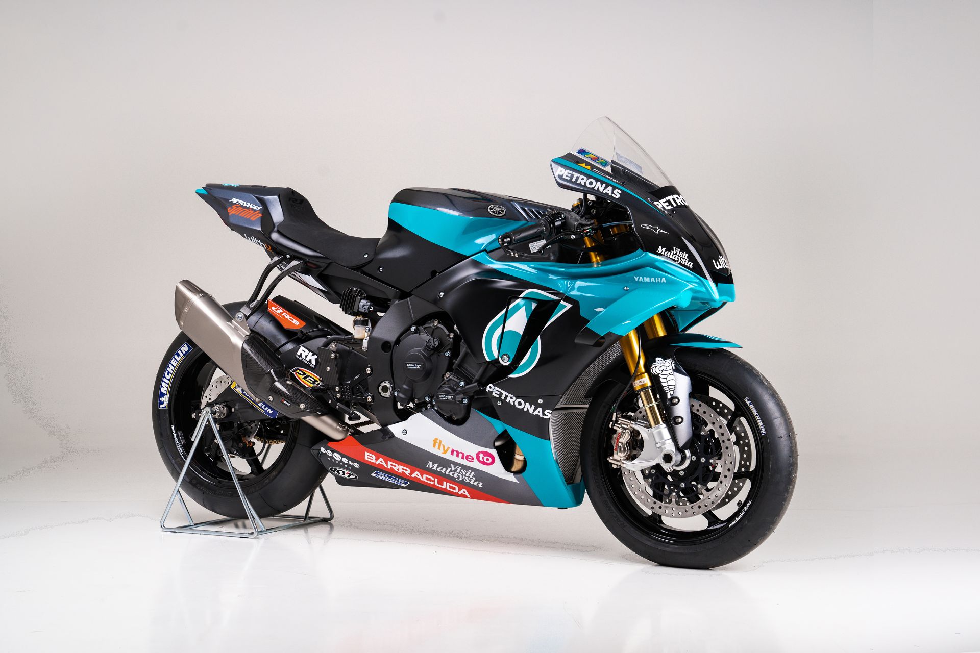 a yamaha yzfr1 motorcycle, the official race bike of the petronas yamaha sepang racing team, is shown in the image. the motorcycle is a blue and black color scheme with various sponsors such as petronas, flyme, barracuda, and michelin.