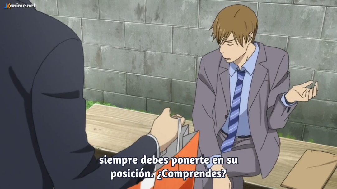 a still from an animated film or series, showcasing two men on a bench. one man, dressed in a gray suit, gestures as he speaks to the other, who is in a black suit and facing away. the scene takes place outdoors against a simple backdrop of a gray brick wall. the lighting appears to be natural, likely daytime. the perspective offers a side view of the interaction.