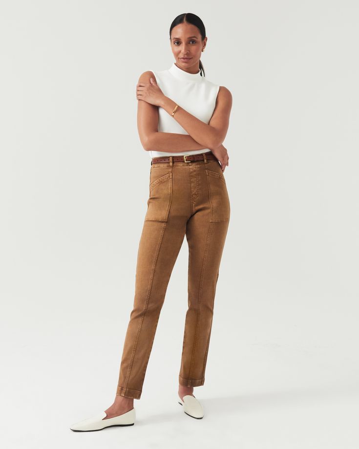 a fullbody studio shot of a woman model wearing a stylish outfit. the outfit consists of a white sleeveless mock neck top and brown highwaisted straightleg pants with utility pockets. the pants have a slim fit and a caramellike brown color. she is also wearing white slipon loafers. the background is plain white, which allows the outfit to stand out. the overall look is minimalist, elegant, and sophisticated.