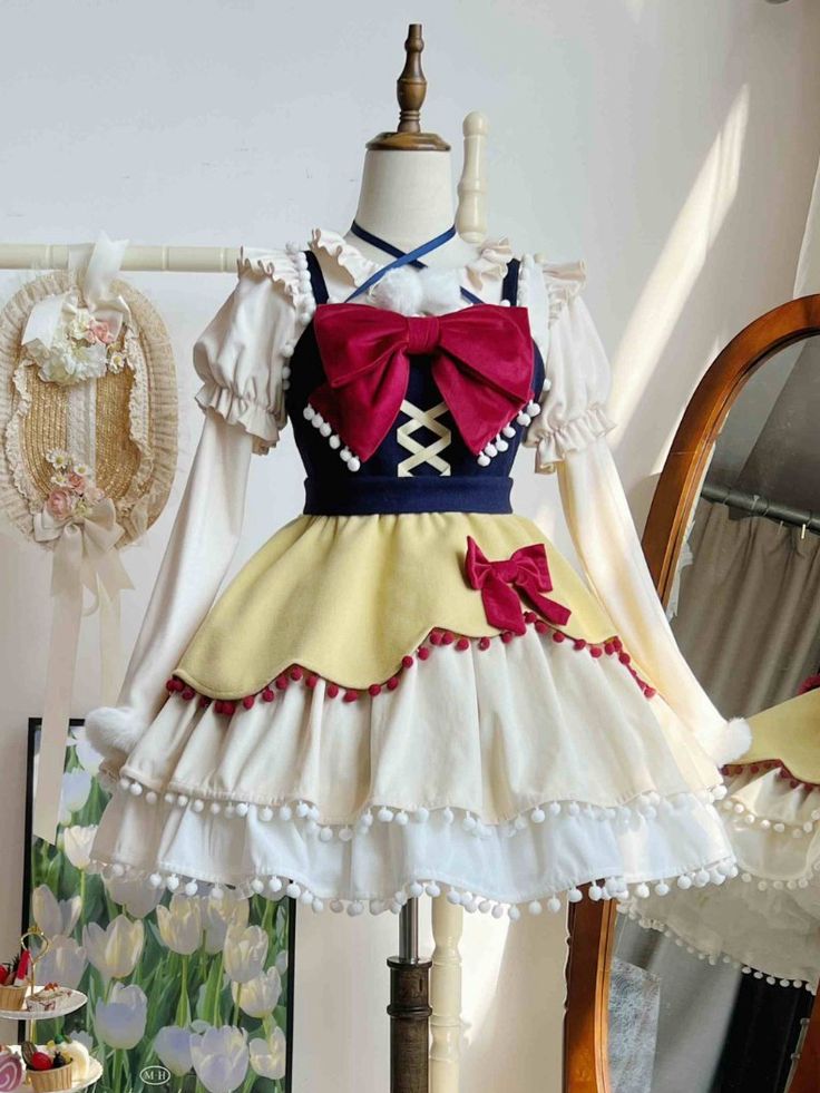 a snow whiteinspired lolita fashion dress is displayed on a mannequin. the dress features a yellow skirt with red and white pompom trim, a navy blue bodice with a large red bow, and white puffed sleeves.  the dress is accessorized with a red ribbon tied in a bow at the waist. the background includes a floral painting, a mirror, and a straw hat.
