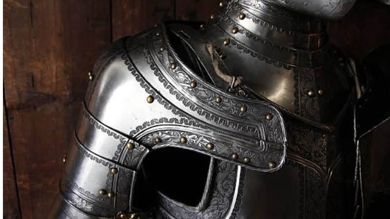 a closeup view of the upper torso of a decorative suit of plate armor, highlighting the intricate details and craftsmanship.  the cool metallic tones and dramatic lighting emphasize the weight and strength of the armor.