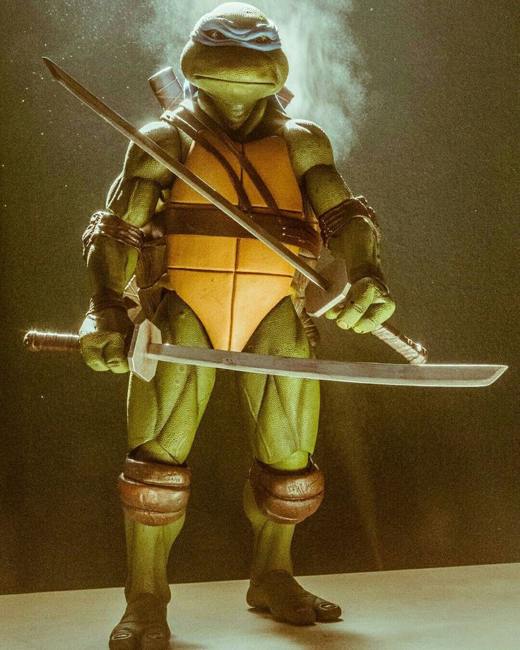 a closeup shot of a leonardo action figure,  from the teenage mutant ninja turtles franchise. he stands in a dramatic pose holding two katanas.  he is  ready for battle!