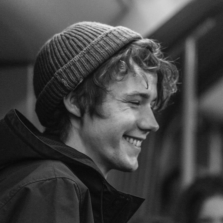 a young man with a beanie and jacket, he is smiling with a big grin and looks happy. he is in an outdoor setting and seems to be enjoying the moment.