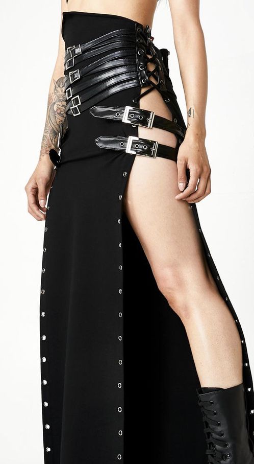 a woman is wearing a highwaisted black skirt with a high slit. the skirt is decorated with grommets along the edges of the slit and has multiple leather belts with buckles around the waist. the skirt also has a corsetstyle lacing detail at the top. the woman is wearing a black boot on her right leg.