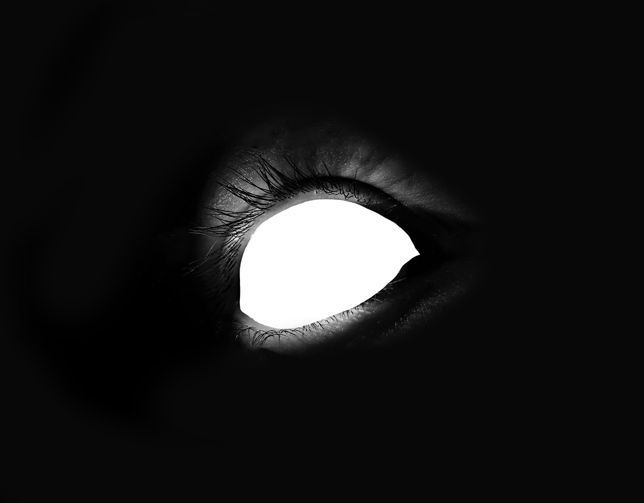 a closeup black and white image of a human eye with a dark, shadowed appearance. the focus is on the eyelashes and the dark pupil.