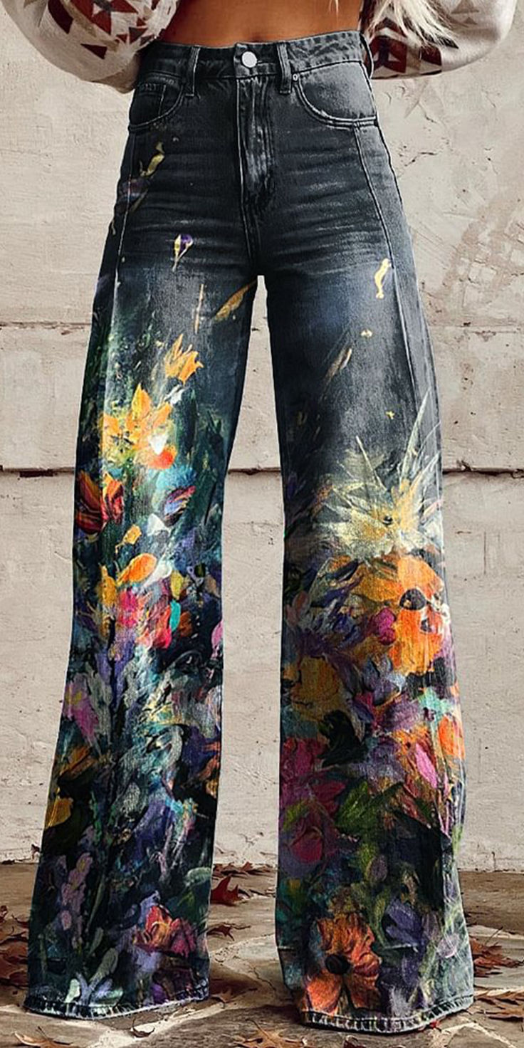 a woman wearing wide leg jeans with floral paint splatters, a relaxed fit with a high waist. the jeans are a dark wash denim and feature colorful, abstract floral designs. the woman is standing in a casual pose, with her arms relaxed at her sides. the jeans are a statement piece, adding a touch of whimsy and style to any outfit. the image is a closeup shot of the woman's legs, showcasing the details of the jeans.  the background is a wall that is textured with a stucco finish, creating a subtle contrast to the smooth surface of the denim.