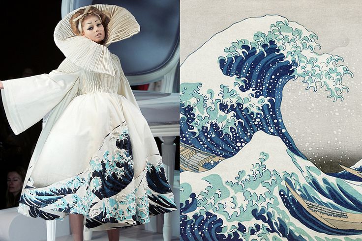 a fashion model wearing a white dress with the great wave off kanagawa printed on the hemline of the skirt. the dress has a dramatic collar and sleeves. the model is walking down a runway. the great wave off kanagawa is a famous japanese woodblock print by hokusai.