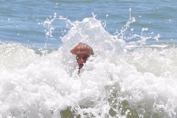 a man is swimming in the ocean as a wave crashes over his head. the water is a beautiful blue color and the sun is shining brightly.