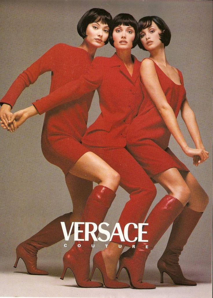 three models, wearing red dresses, are posing in a studio. they are all wearing red kneehigh boots and high heels.  the woman in the center is wearing a red suit. the woman on the left is wearing a red dress, and the woman on the right is wearing a red sundress. the photo is a fashion advertisement for versace.
