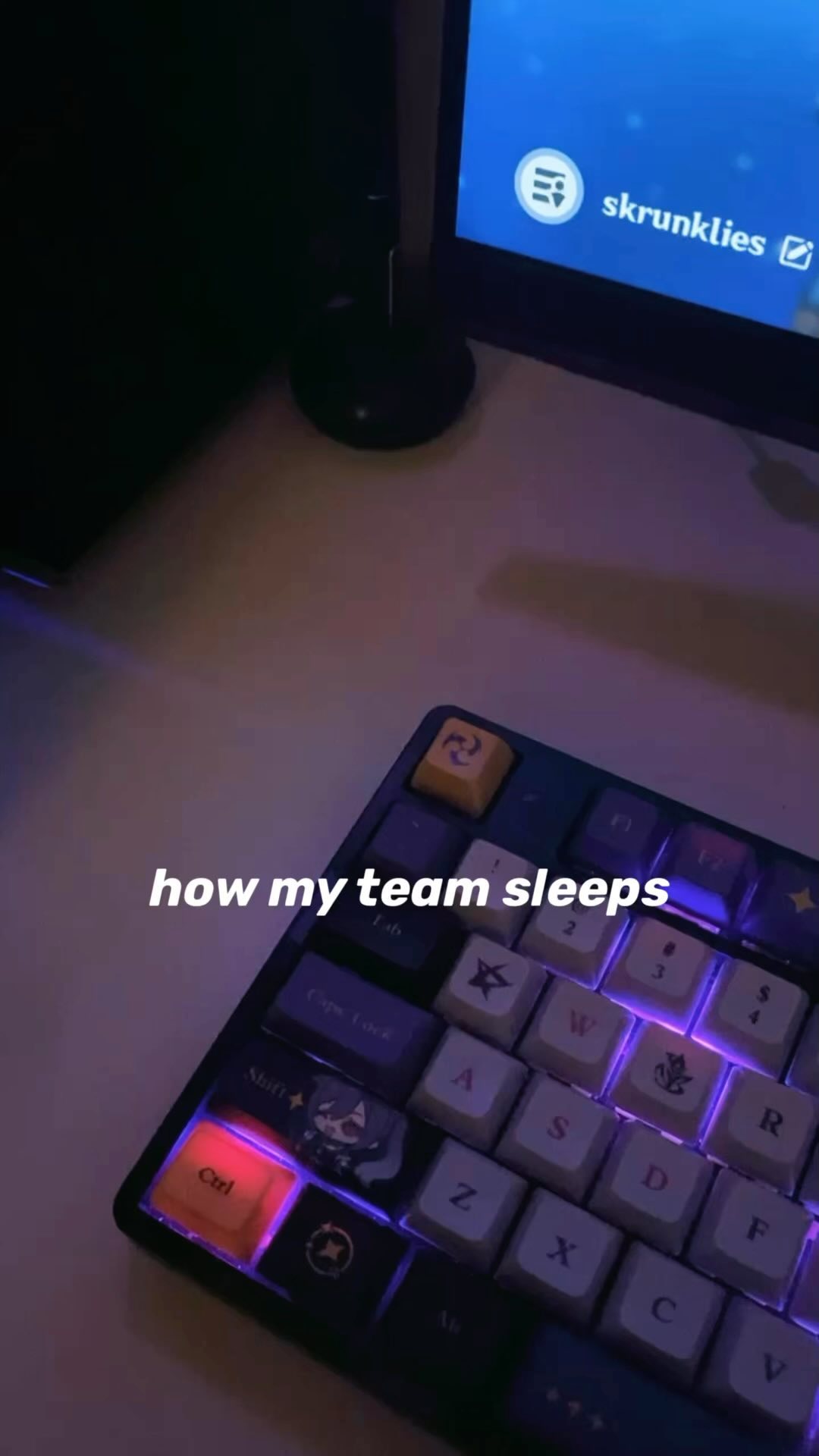 a closeup shot of a custom mechanical keyboard with purple backlighting. the keyboard is partially visible, and the caption "how my team sleeps" is overlaid on the image. in the background, a computer monitor displays the word "skrunklies."  the overall scene suggests a gaming or computer setup at night.