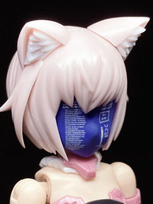 a close up of a pink anime doll figurine with cat ears. the doll is wearing a blue and white mask and a pink and white collar. the figurine has white hair and is posed in a way that suggests it is looking directly at the camera.