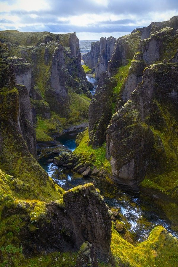 a stunning landscape photograph capturing the fjadrargljufur canyon in iceland. the image showcases the deep canyon with mosscovered rocks and cliffs, a river flowing through the center, and a cloudy sky in the background. the scene is vibrant with green hues and emphasizes the natural beauty of the icelandic landscape.