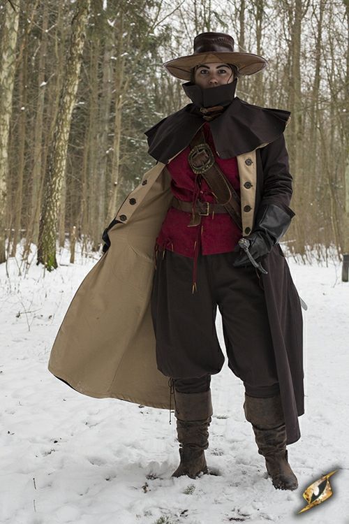 a woman in a  fantasy costume stands in a snowy forest. she is wearing a long brown coat, a red vest, a black mask, and a widebrimmed hat. her boots are brown and leather.  the snow is all around her.  she looks out towards the camera with a confident expression.