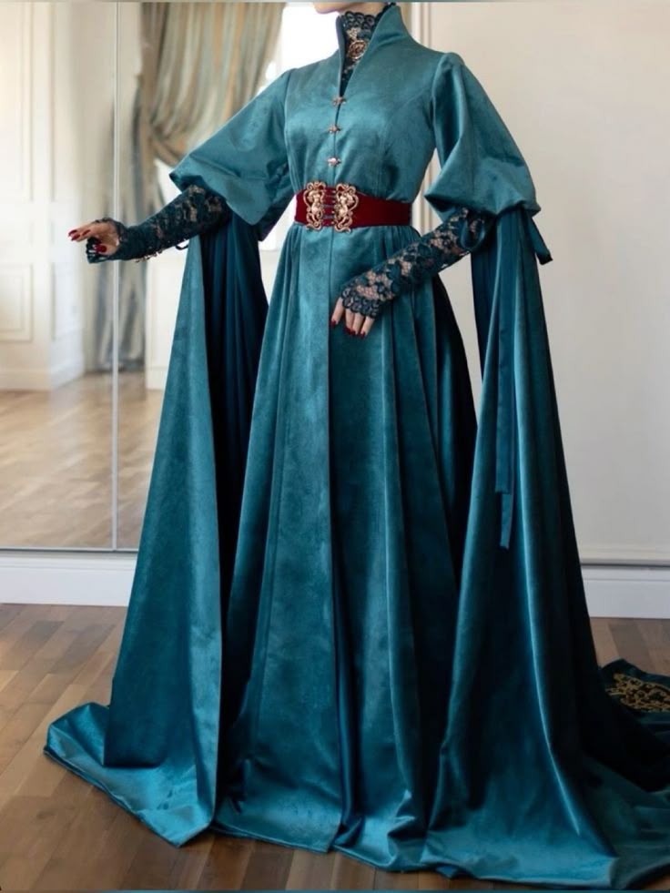 a person is wearing a floorlength teal velvet gown with long, flowing sleeves and lace sleeves underneath. the gown features a high collar and is cinched at the waist with a wide red belt. the gown has a medieval or renaissance style.