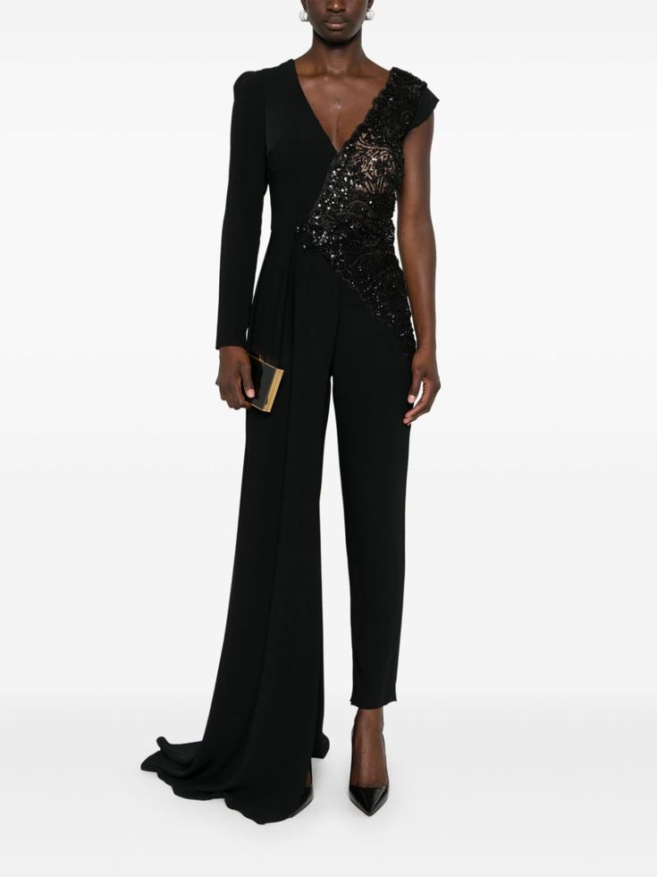 a woman is wearing a black oneshoulder jumpsuit with sequins and a long train. she is also wearing black high heels and holding a small black clutch.